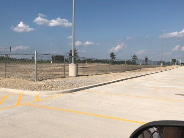 A parking lot with a fence and a pole in the background