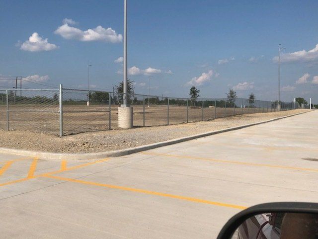 A parking lot with a fence and a pole in the background