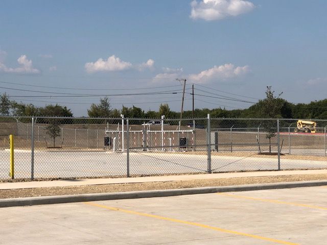 A chain link fence surrounds a basketball court in a parking lot