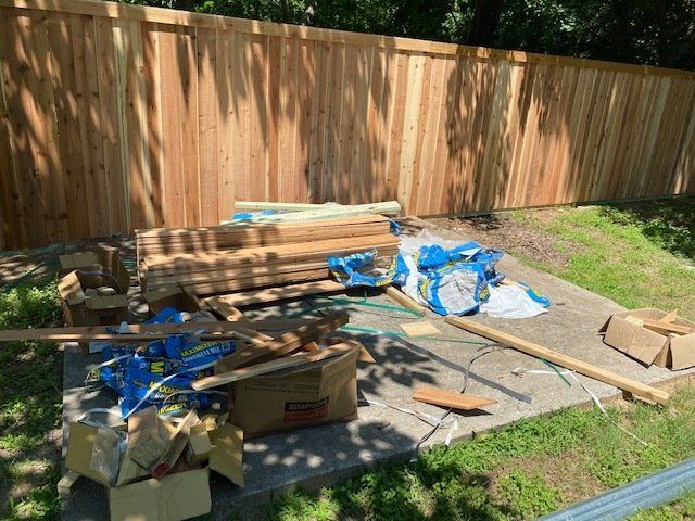 A pile of wood is sitting on the ground in front of a wooden fence.