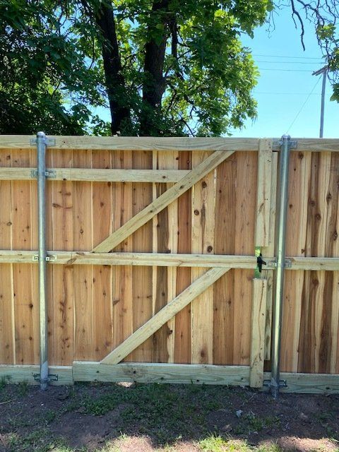 A wooden fence with a metal gate and trees in the background