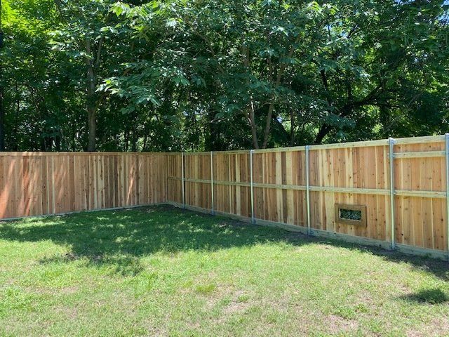 A wooden fence surrounds a lush green yard with trees in the background.