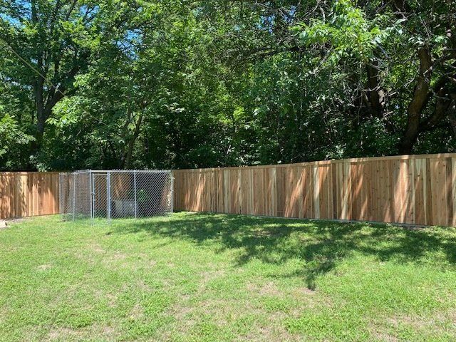 A wooden fence surrounds a lush green yard with trees in the background.
