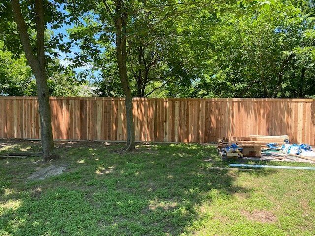 A wooden fence is being built in a backyard surrounded by trees.