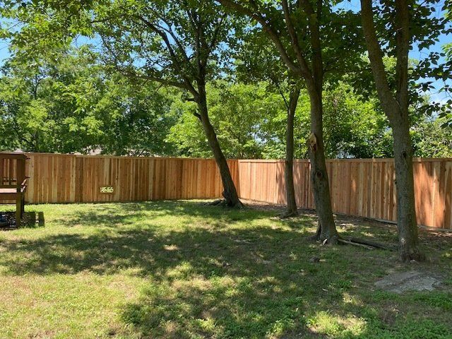 There is a wooden fence in the backyard surrounded by trees.