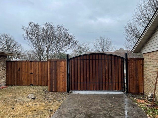 A wooden fence with a metal gate in front of a house.