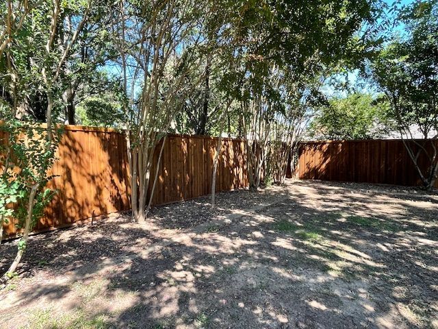 A wooden fence is surrounded by trees in a backyard.