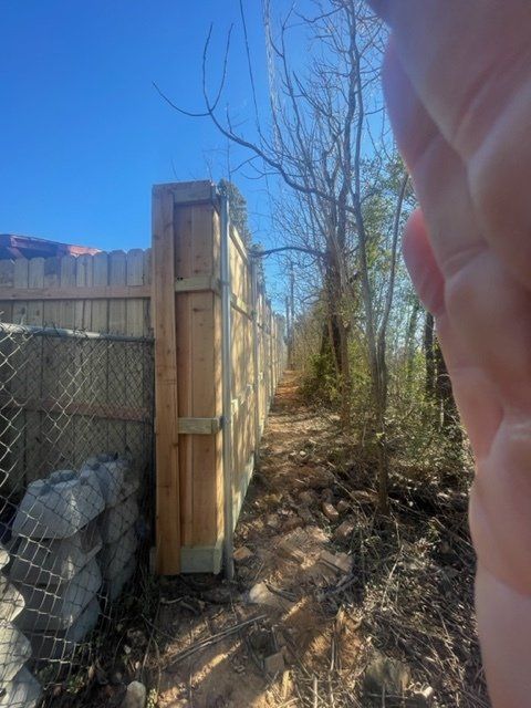 A person is standing next to a wooden fence in the woods.