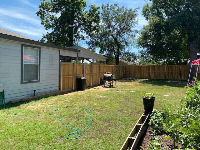 The backyard of a house with a wooden fence and a grill.