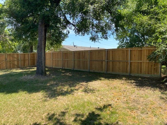 A wooden fence is surrounded by trees in a backyard.