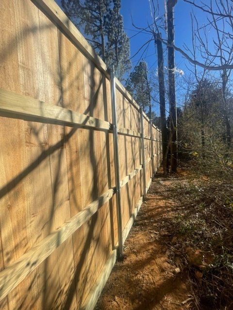 A wooden fence surrounds a dirt path in the woods.