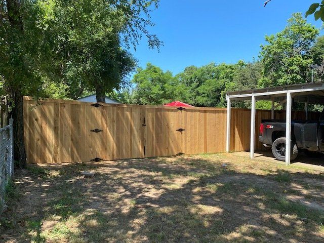 A wooden fence is surrounding a carport with a truck parked underneath it.