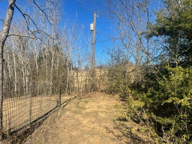 A dirt path going through a fenced in area with trees and a telephone pole.