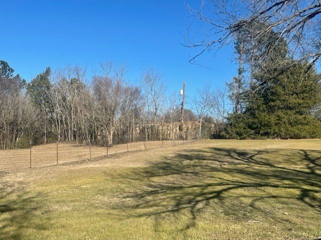A large grassy field with trees in the background and a fence in the foreground.