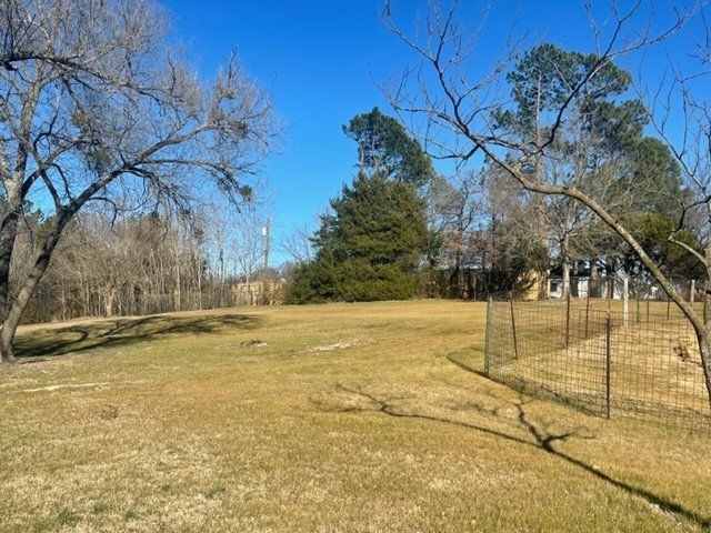 A large grassy field with a fence and trees in the background.