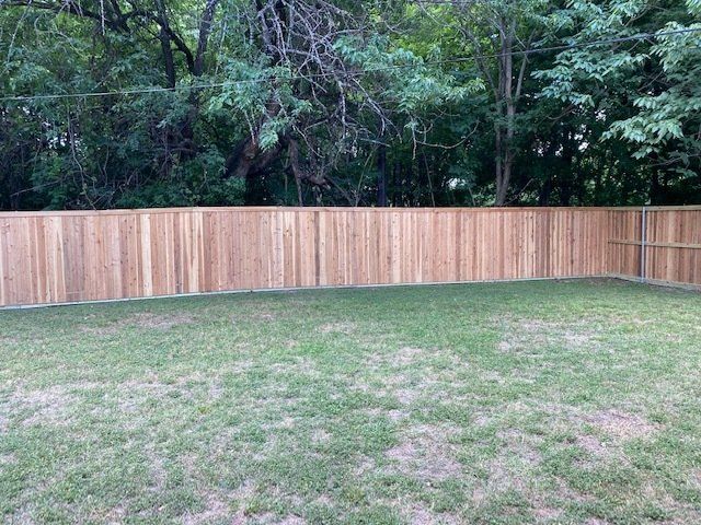 A wooden fence surrounds a lush green lawn in a backyard.