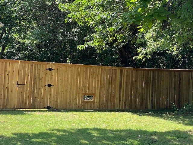 A wooden fence with a gate in the middle of a lush green field.