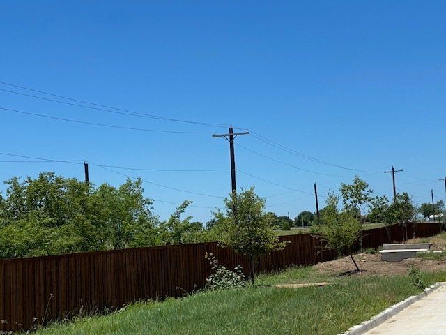 A wooden fence surrounds a grassy area with trees and power lines.