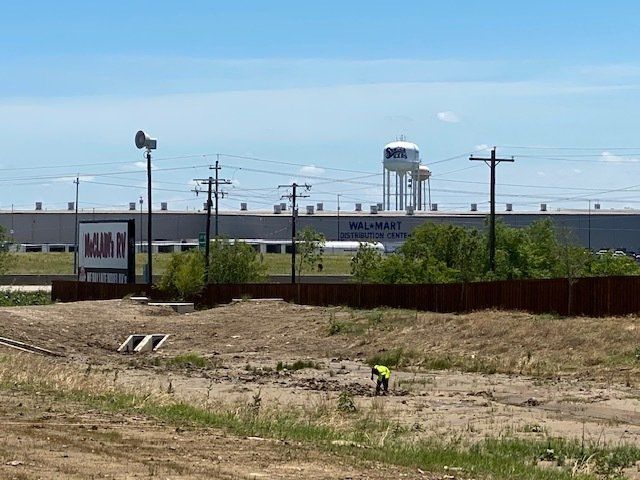 A man is working in a field in front of a large building.