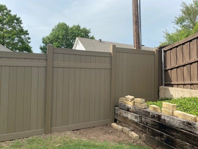 A tan fence is sitting next to a brick wall in a backyard.