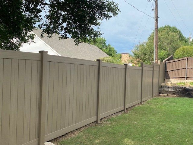 A tan fence surrounds a lush green yard in front of a house.