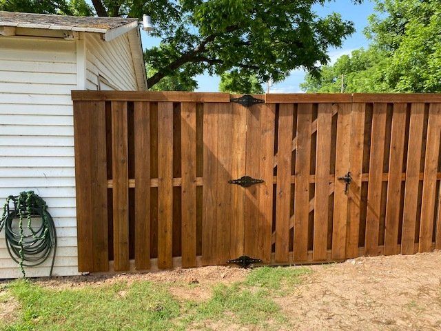 A wooden fence with a gate is in front of a white house.