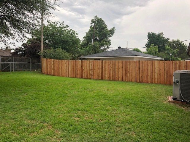 A wooden fence surrounds a lush green yard with a house in the background.