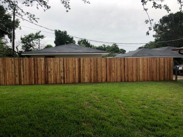 A wooden fence surrounds a lush green yard in front of a house