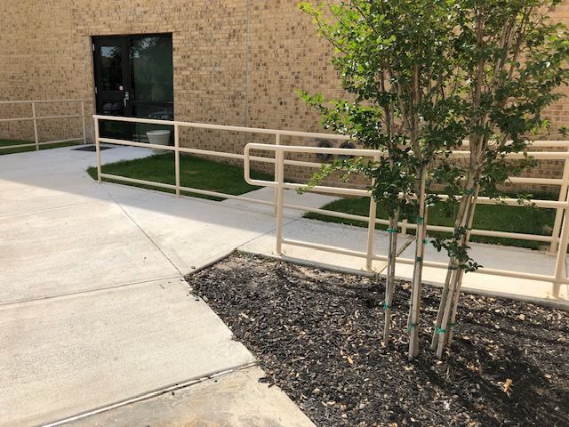 A ramp with a railing and a tree in front of a building.