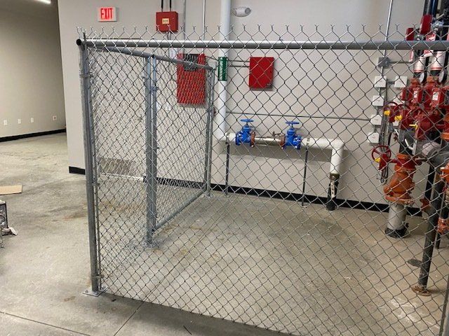 A chain link fence is surrounding a room with pipes and valves.
