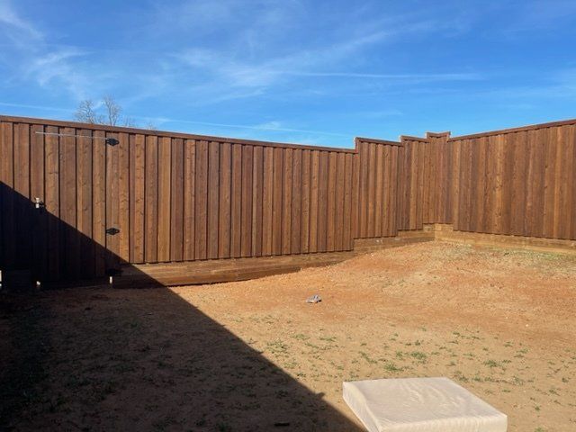 A wooden fence is in the middle of a dirt yard.
