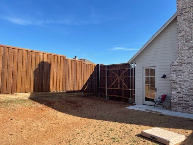 A backyard with a wooden fence and a white house