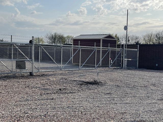 A chain link fence is surrounding a gravel area with a shed in the background.