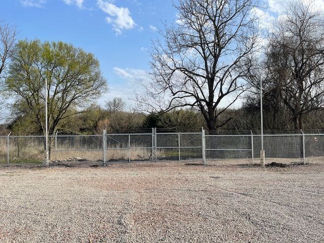 A chain link fence surrounds a gravel area with trees in the background.