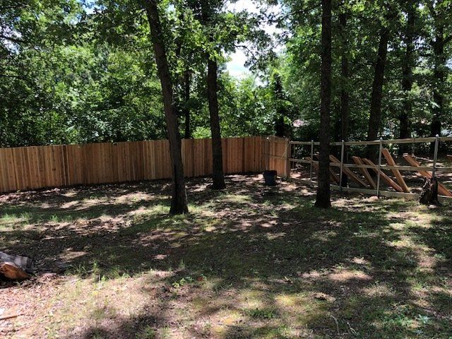 A wooden fence is surrounded by trees in a backyard.