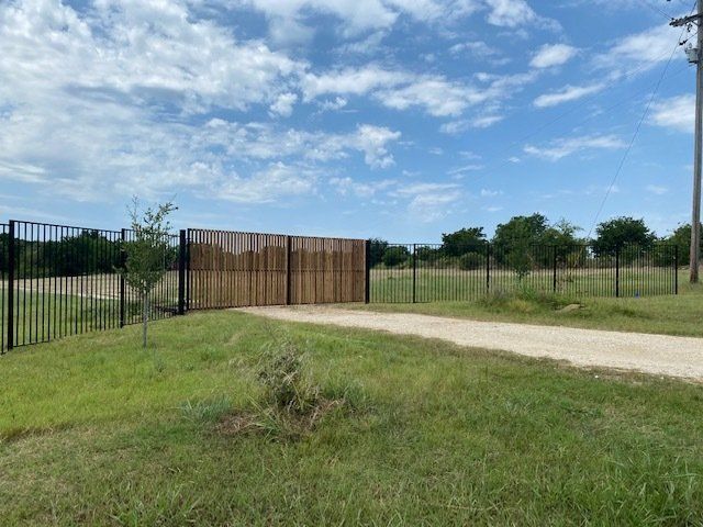 A wooden gate is surrounded by a metal fence and a dirt road.