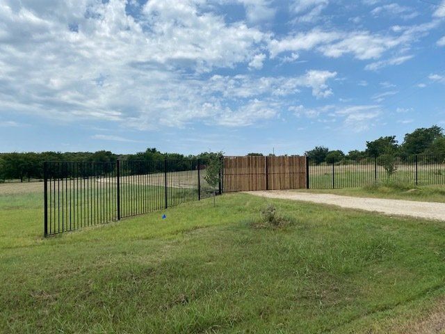 A fence surrounds a grassy field and a dirt road.