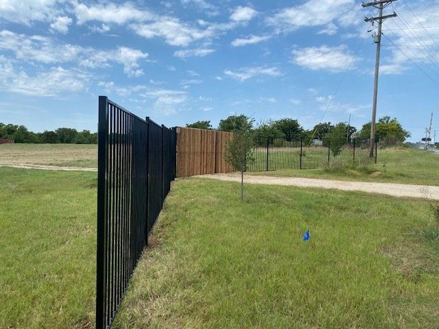 A black fence surrounds a grassy field with a wooden fence in the background.
