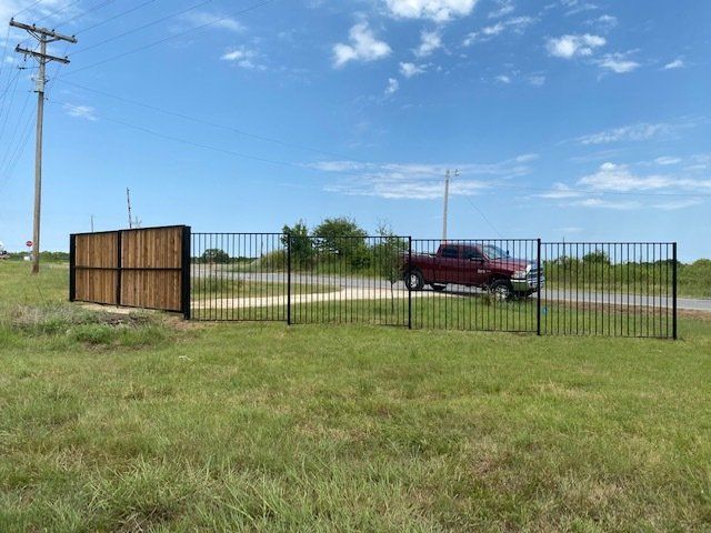 A red truck is parked behind a fence in a grassy field.