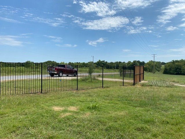 A red truck is parked in a grassy field next to a fence.