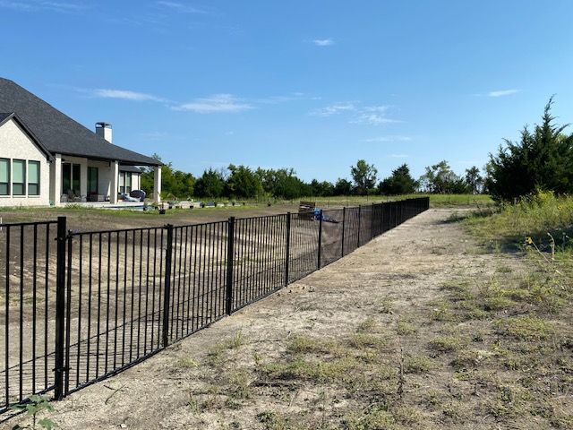 A black fence surrounds a dirt road in front of a house