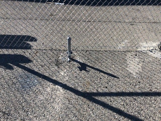 A shadow of a person is cast on the ground next to a chain link fence.