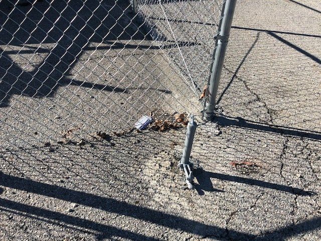 A chain link fence with a broken post and a can on the ground
