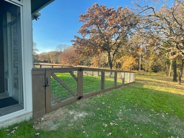 A fence surrounds a lush green field in front of a house.