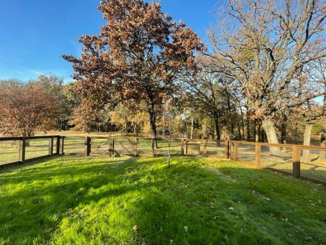 A wooden fence surrounds a grassy field with trees in the background.