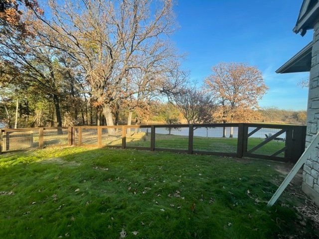 A backyard with a wooden fence and a lake in the background.