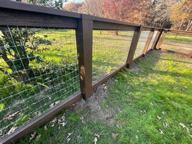 A wooden fence with a wire fence surrounding a grassy field.