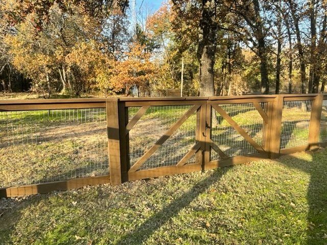 A wooden fence with a gate is surrounded by grass and trees.