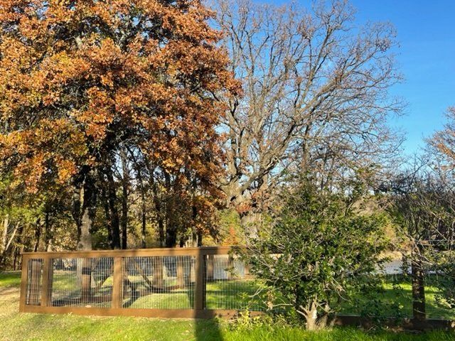 A wooden fence is surrounded by trees and grass in a park.