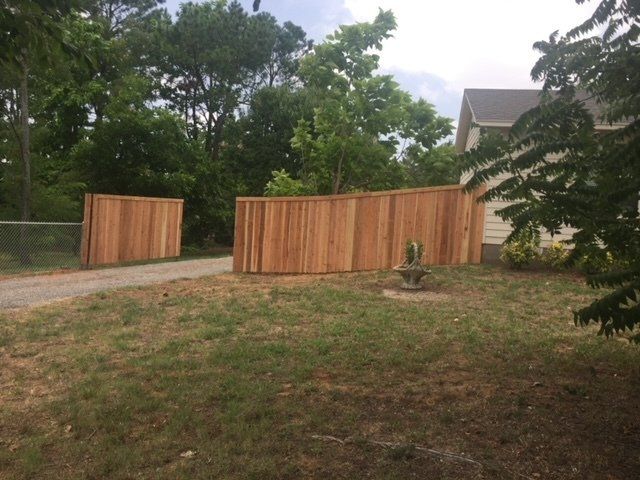A wooden fence surrounds a grassy yard in front of a house.